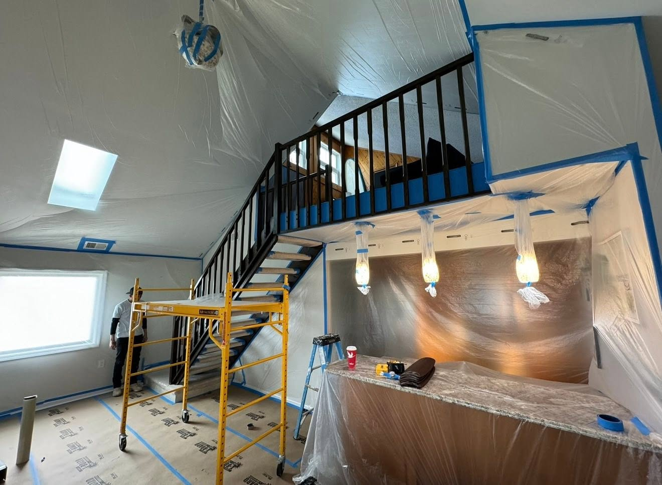 Interior renovation with protective plastic sheeting, metal staircase, scaffolding, and work supplies