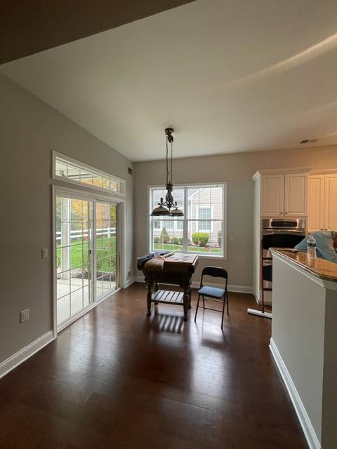 Modern kitchen and dining area with dark hardwood floors, white cabinetry, and large windows overlooking backyard