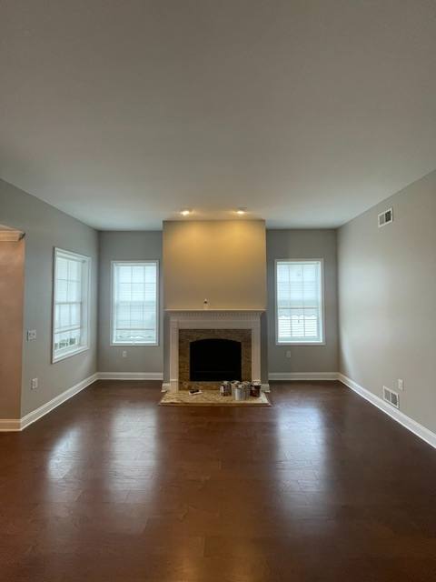 Empty living room with fireplace, hardwood floors, and windows with shutters