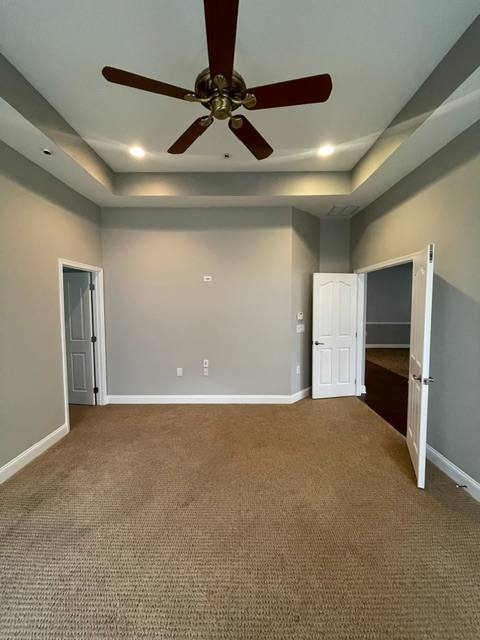 Empty bedroom with brown carpet, tray ceiling, ceiling fan, and two white closet doors