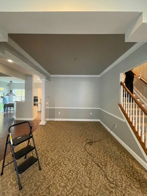 Empty room with beige carpet, two-tone gray and white walls, wooden railing, and folding chair