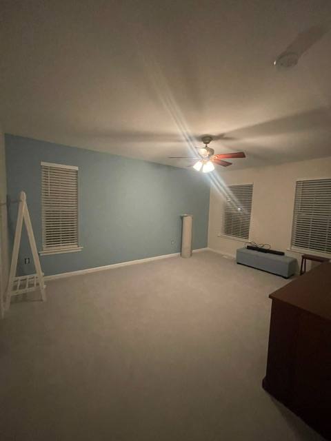 Empty room with blue accent wall, ceiling fan, louvered windows, and wooden furniture