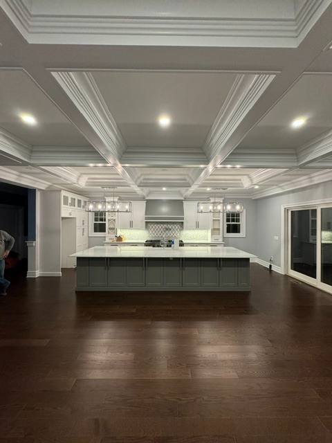 Modern kitchen with white cabinetry, dark island, coffered ceiling, and hardwood floors