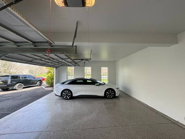 White sedan parked in modern garage with open door and dark SUV visible outside
