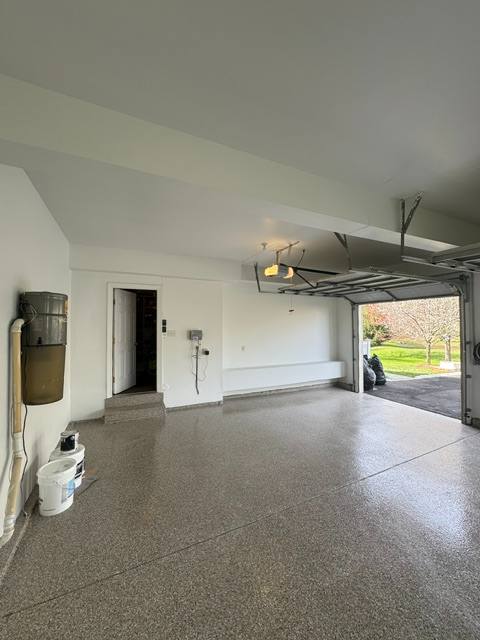 Spacious empty garage interior with epoxy flooring, open garage door, and natural lighting