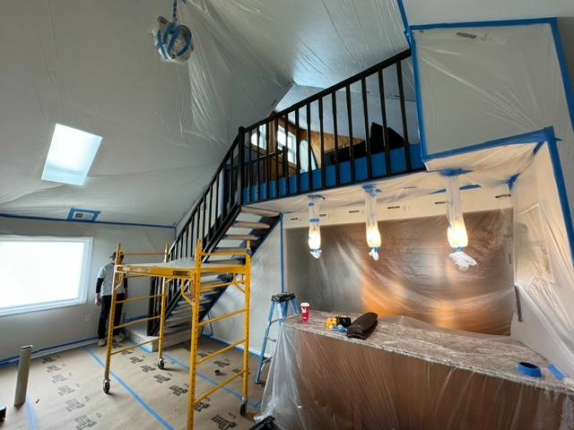 Interior renovation in progress with protective plastic sheeting and metal staircase