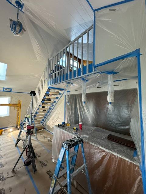 Interior renovation in progress with plastic sheeting, blue framing, and staircase under construction