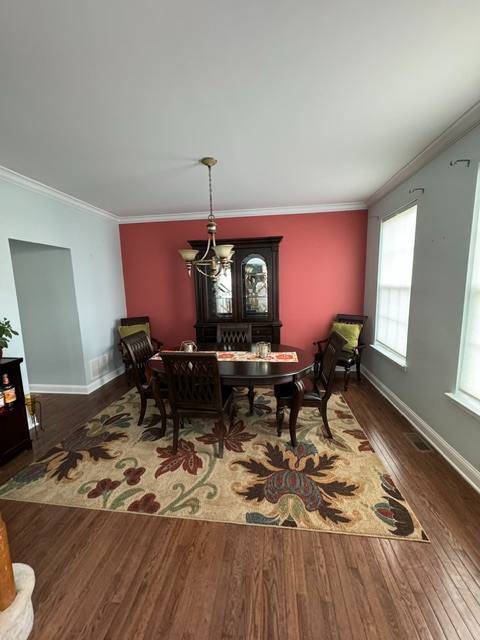 Formal dining room with red accent wall, round dark wood table, four chairs, ornate cabinet, and patterned area rug