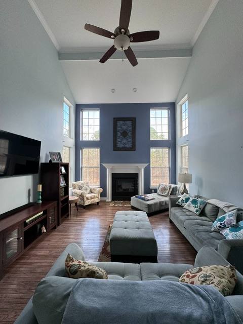 Modern living room with high ceilings, ceiling fan, fireplace, large windows, and gray seating furniture