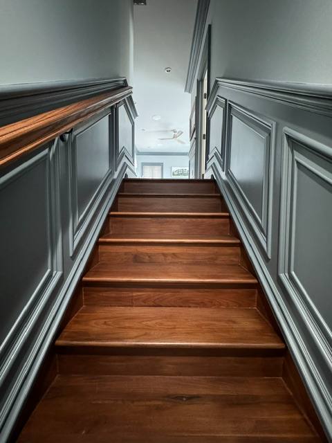 Wooden staircase with gray paneled walls and wooden handrails leading upward