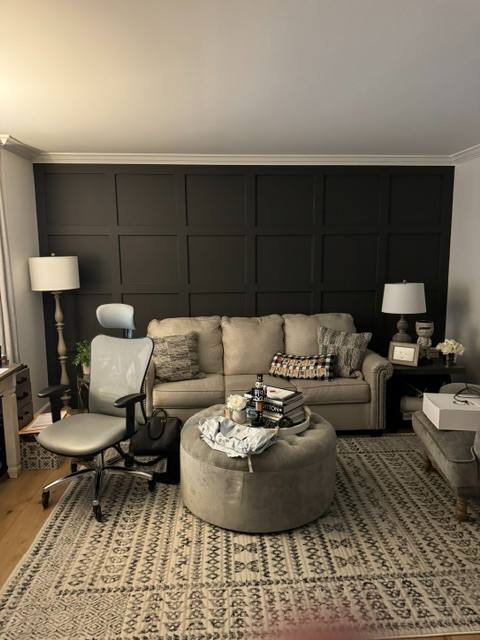 Modern living room with beige sofa, round ottoman, desk chair, black paneled accent wall, and neutral décor