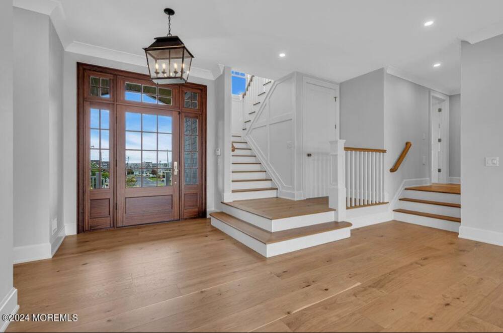 Bright foyer with wide plank wood flooring, dual staircases, white walls, and French doors with water view