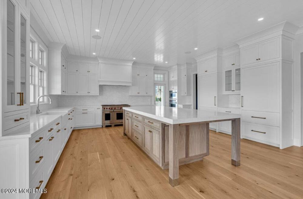 Modern luxury kitchen with white cabinetry, wood island, stainless steel appliances, and hardwood flooring