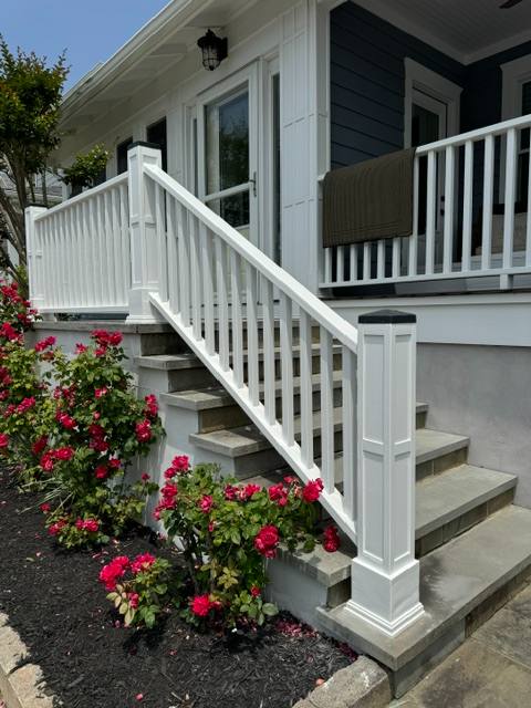 White deck railing and stairs with pink flowers and dark siding house entrance