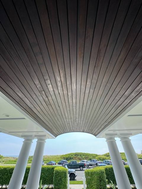 Covered carport with white columns and striped metal ceiling overlooking parking lot and landscaped grounds