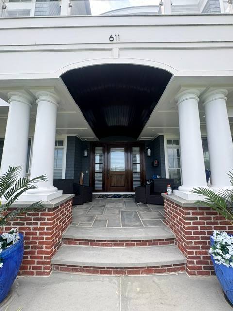Front entrance of 611 with white columns, black awning, wooden door, and brick planters with flowers