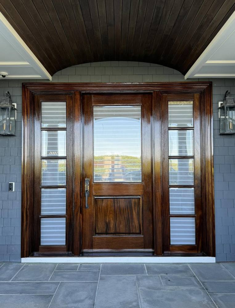 Dark wood entry door with sidelights and transom window on stone patio