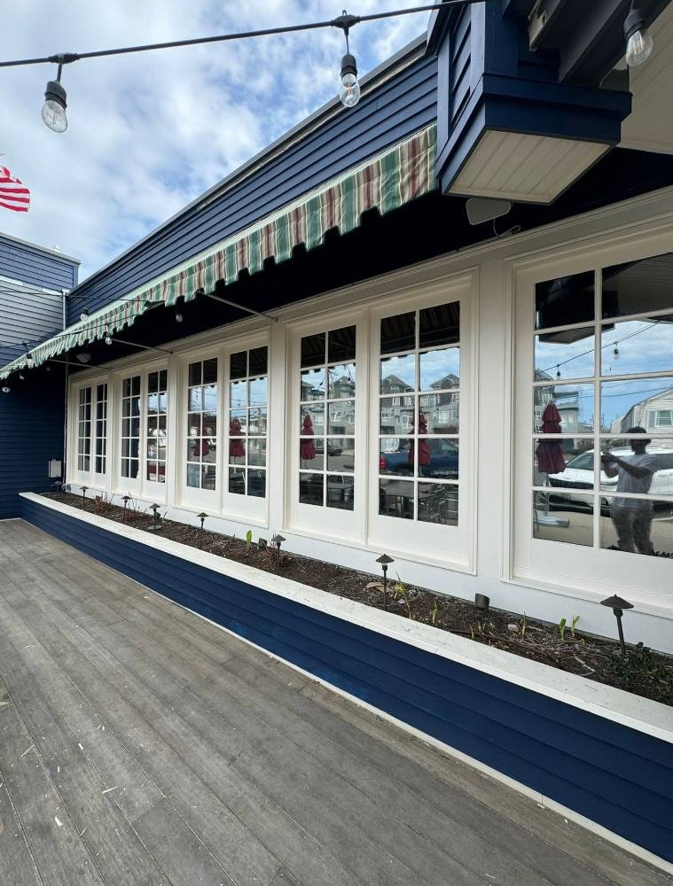 Modern storefront with navy blue siding, white multi-pane glass doors, striped awning, and American flag