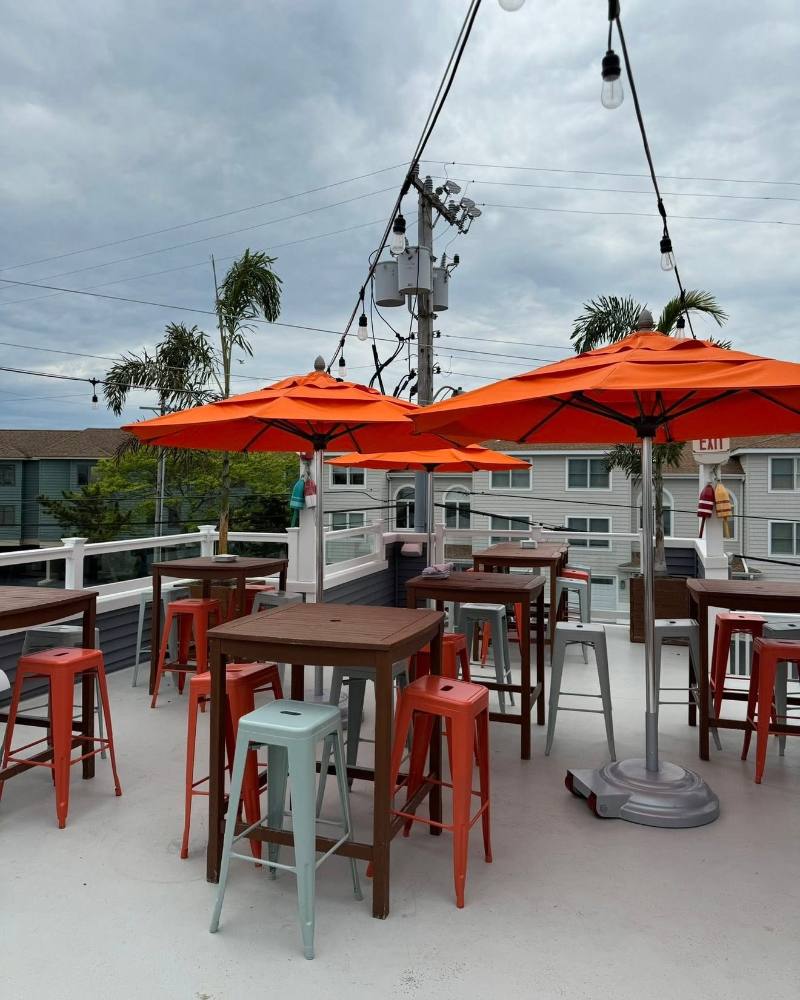 Rooftop patio with orange umbrellas, wooden tables, and red metal stools overlooking residential buildings
