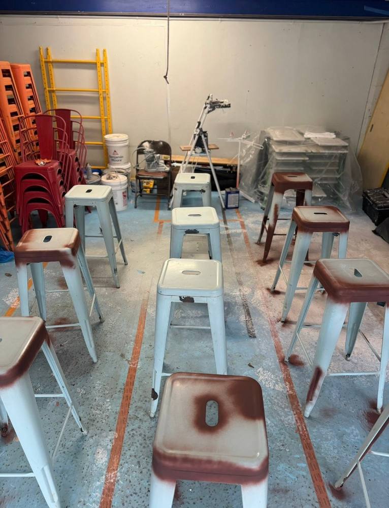 Industrial warehouse with metal bar stools arranged in rows during refinishing process