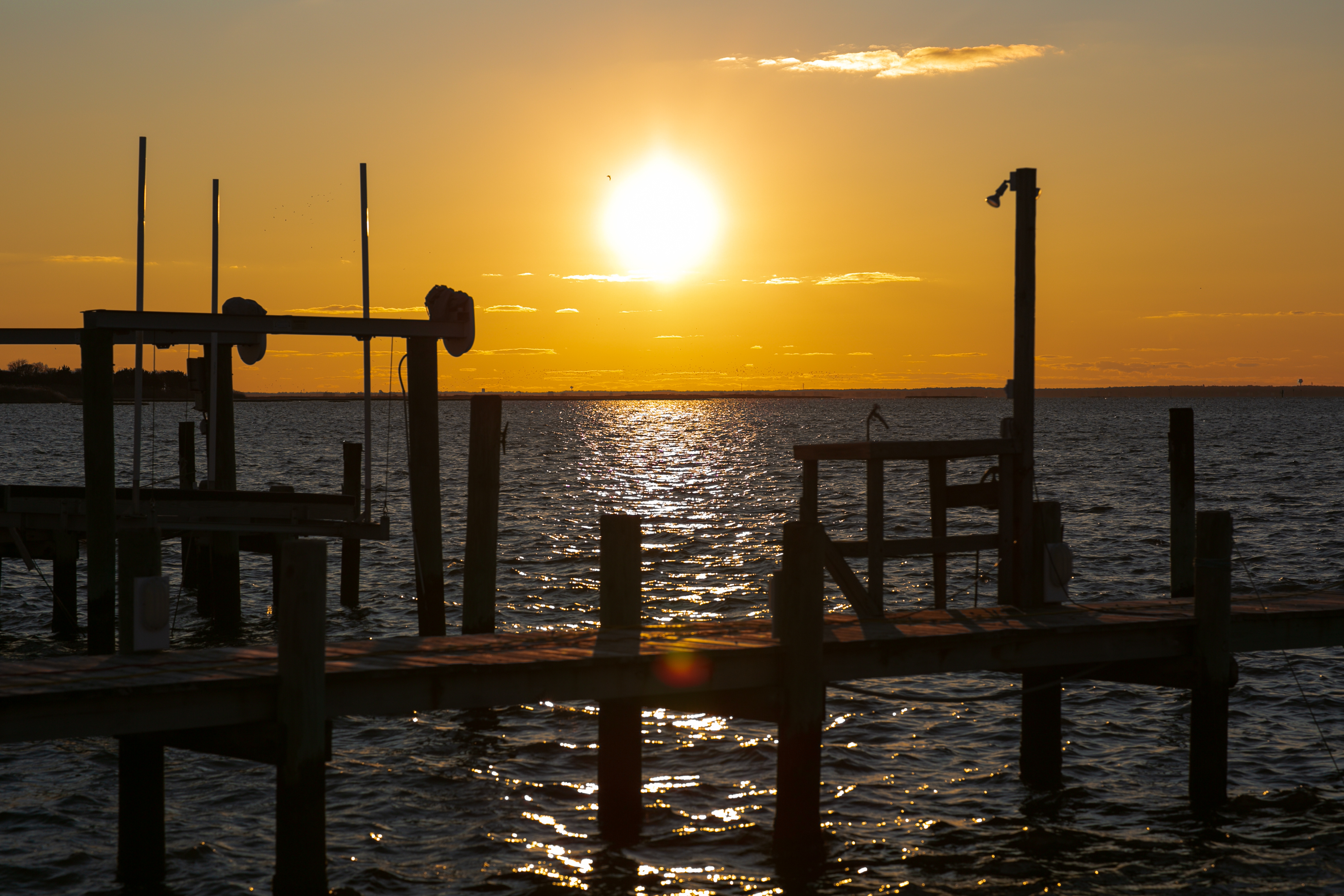 Wooden pier structure silhouetted against golden sunset over calm water