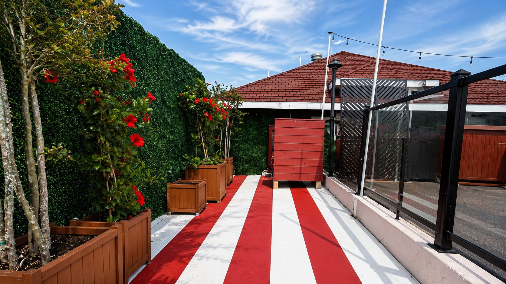Modern rooftop terrace with red and white striped flooring, ivy-covered walls, and flowering plants