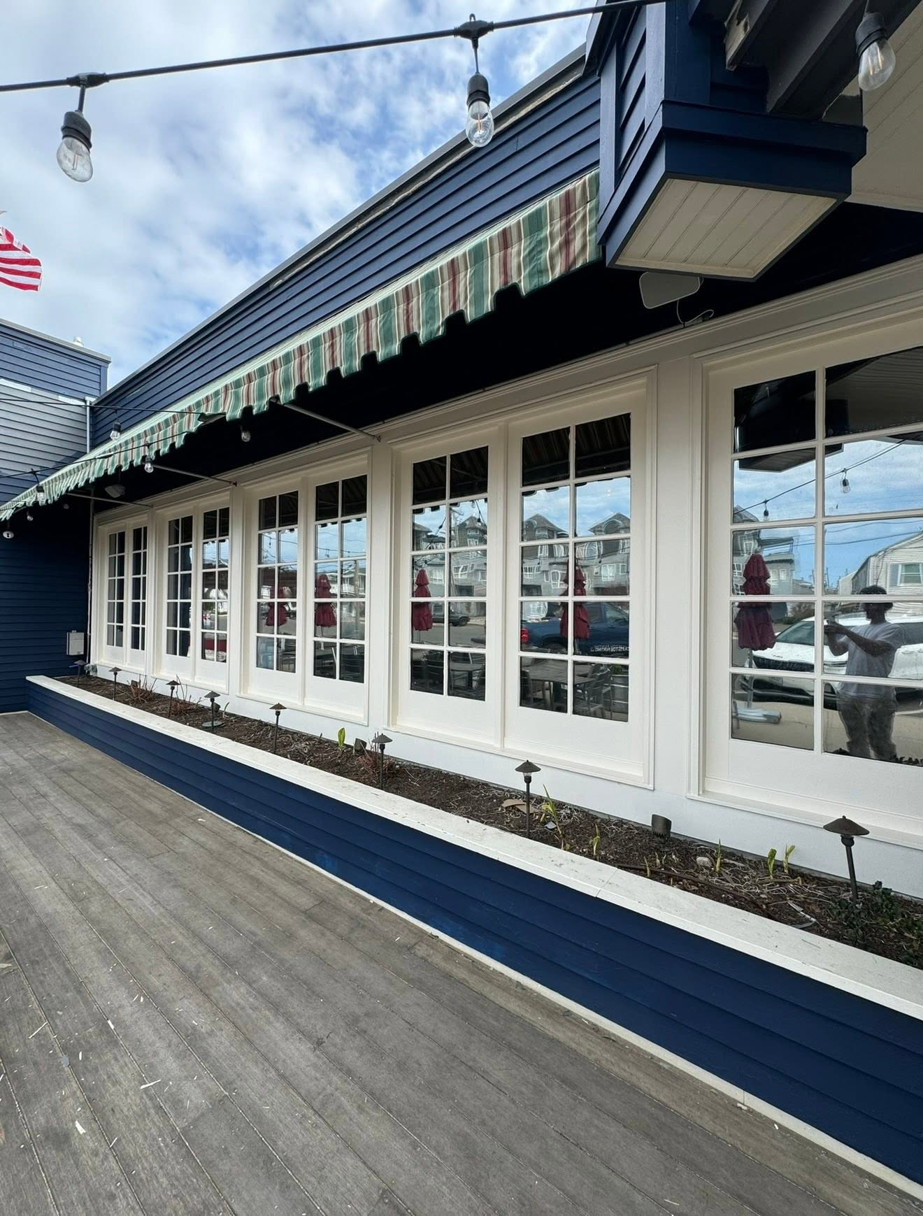 Modern coastal storefront with white French doors, striped awning, and blue siding