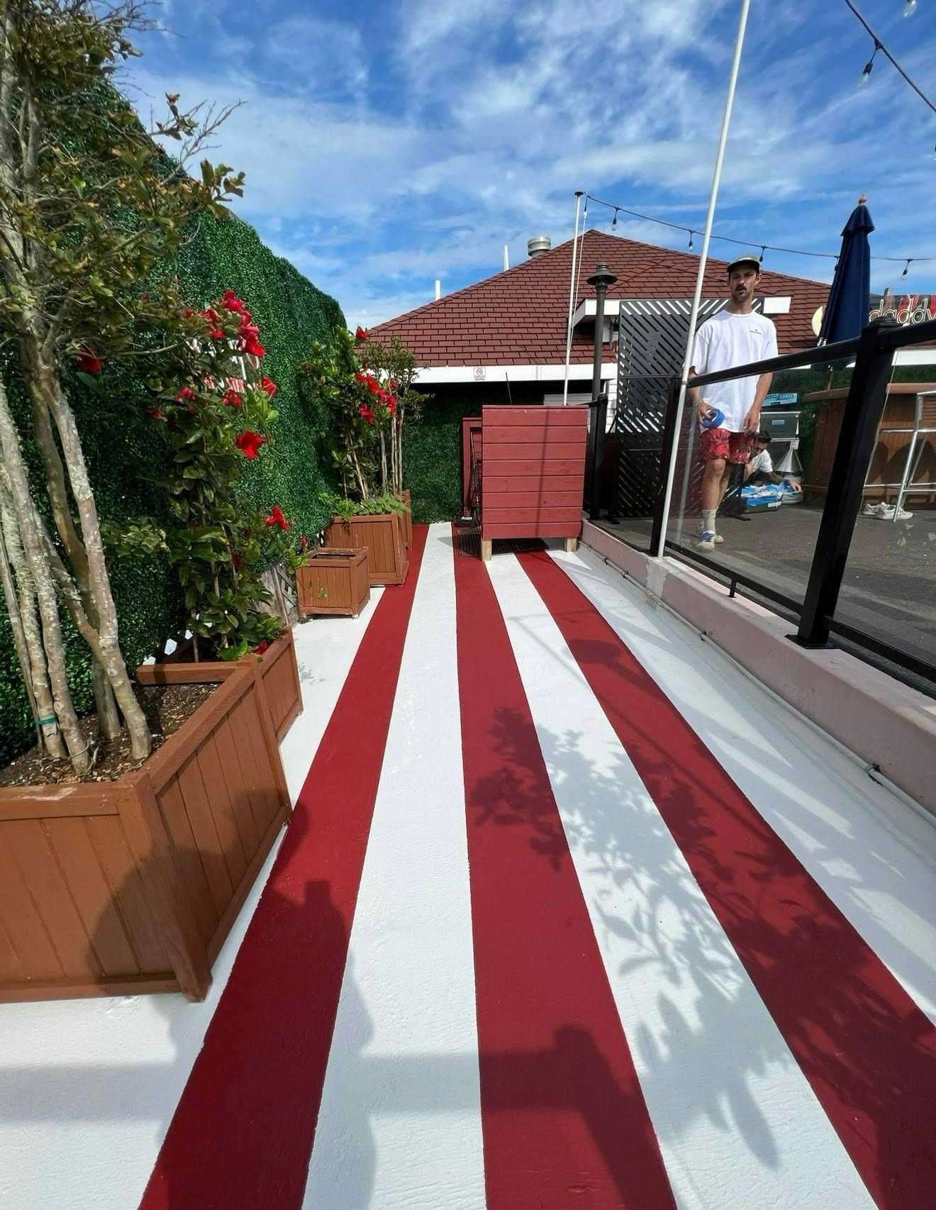 Red and white striped outdoor patio with ivy-covered wall, red flowers, and modern house
