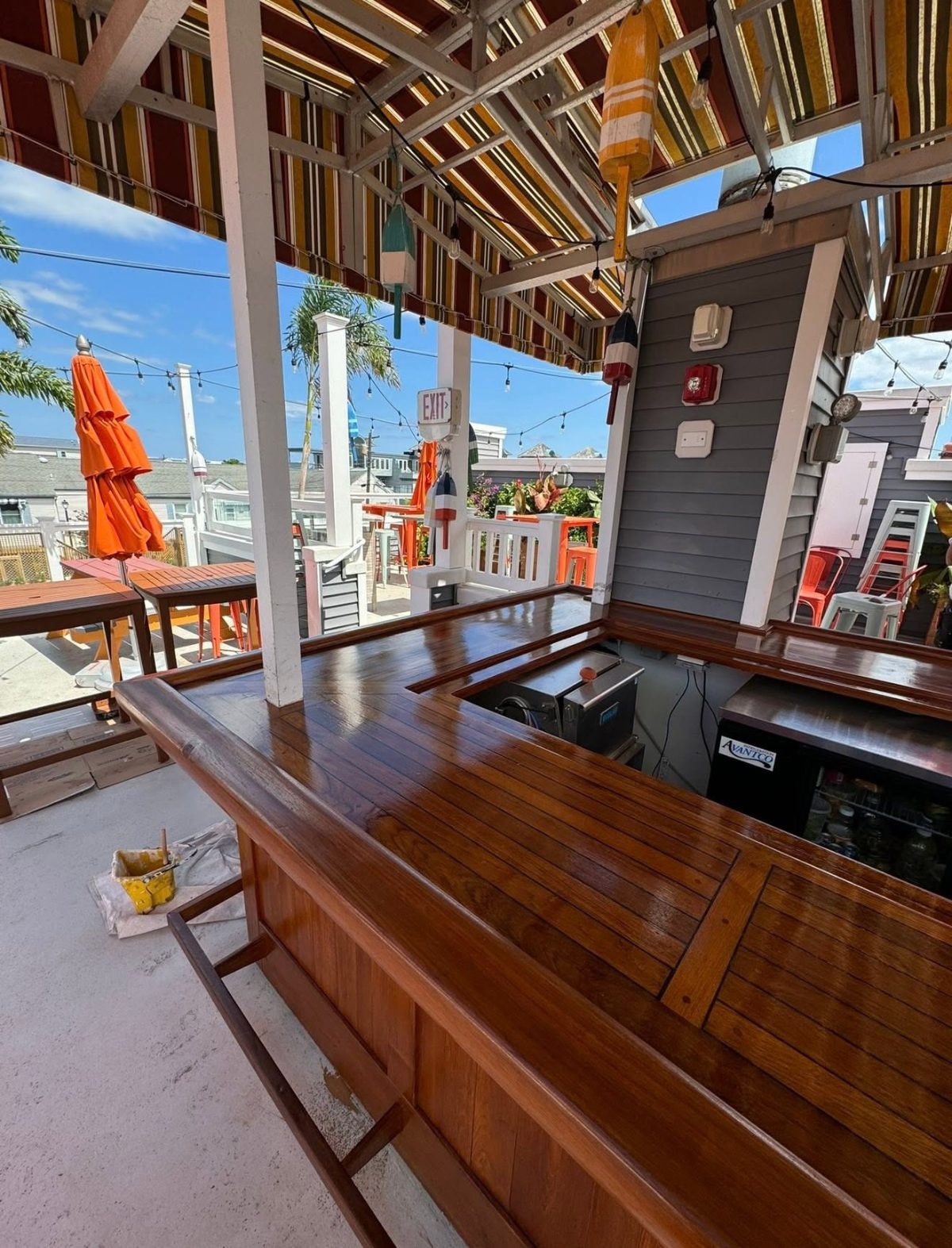 Rooftop bar with wooden counter, orange umbrellas, and coastal town views under pergola shade